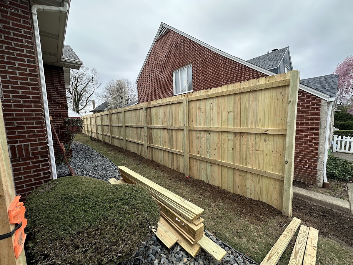 A new wood privacy fence installed by AE Home Improvements, with fresh lumber staged for the next section of the job